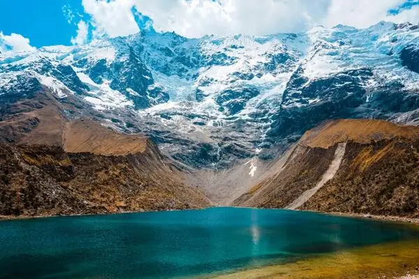 Backpackers hiking to Humantay Lagoon in Cusco with turquoise water and snowy Andean peaks in the background.