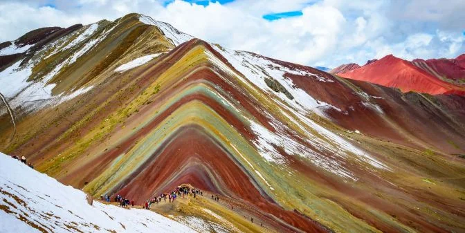 Backpacker at Rainbow Mountain summit with vivid colored layers
